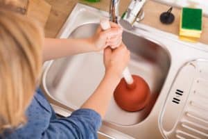 High Angle View Of Woman Using Plunger In Blocked Drain